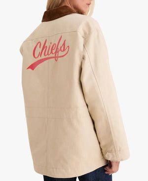 A person shown from the back wearing a beige jacket with a brown collar and a red 'Chiefs' script logo on the back, against a light gray studio background.